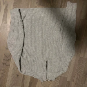 Grå ribbad stickad tröja med zip - Säljer en grå stickad tröja med ribbad struktur och half zip-detalj framtill. Tröjan har långärmade och en klassisk rund hals. Perfekt för dig som gillar enkel och stilren design med lite edge.