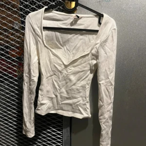 Vit ribbad långärmad topp S - Säljer en vit ribbad långärmad topp med v-ringad hals. Toppen är figurnära och har en enkel, stilren design som passar perfekt till jeans eller kjol. Materialet är mjukt och stretchigt för en bekväm passform.