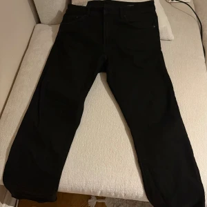 Svarta jeansbyxor i storlek 33/32 - Snygga svarta jeansbyxor från HM i klassisk femficksmodell. Byxorna har rak passform och är tillverkade i ett mjukt bomullsmaterial med lite stretch för extra komfort. Perfekt för dig som gillar stilrena och enkla jeans med modern look.