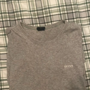Grå t-shirt från Hugo Boss - Säljer en stilren grå t-shirt från Hugo Boss med diskret logga på bröstet. T-shirten har rund halsringning och klassisk passform. Perfekt för dig som gillar enkel och snygg design med premiumkänsla.
