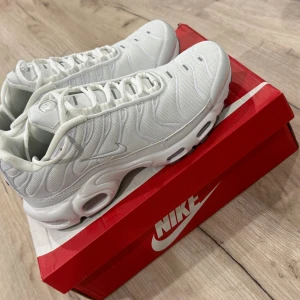 Nike Air Max Plus vita sneakers - Nike Air Max Plus sneakers i helvit färg med mesh och syntetmaterial. Snygga detaljer med Tn Air-logga på hälen, vågiga linjer och synlig Air Max-dämpning i sulan. Rund tå, snörning och platt sula för en clean och sportig look.
