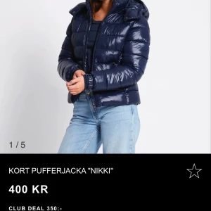Mörkblå kort pufferjacka Nikki - Snygg kort pufferjacka i glansig mörkblå färg från Nikki. Jackan har huva, dragkedja framtill och quiltad design som ger en modern look. Perfekt för kyliga dagar när du vill hålla stilen. säljer pg vill köpa en annan färg s/xs