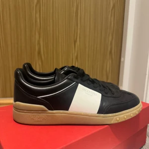 Valentino Garavani sneakers svart/vit - Snygga sneakers från Valentino Garavani i svart skinn med vit panel på sidan och beige sula. Klassisk låg modell med snörning och diskret logga på sidan. Köpta för 8 000 säljer för halva priset