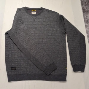 Grå sweatshirt från Camel Active - Säljer en grå sweatshirt från Camel Active med diskret rutmönster i tyget. Tröjan är aldrig använd, köptes för 1198kr på Nisses Herrmode i Malmö. Storlek L.