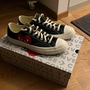 Converse x Comme des Garçons sneakers - Svarta Converse sneakers i samarbete med Comme des Garçons, med ikoniskt rött hjärta med ögon på sidan. Klassisk låg modell med vit tå och sula, vita snören och kontrasterande sömmar. Ovandel i slitstark bomull och platt gummisula. Perfekt för dig som gillar unik streetstyle. Dom är köpte på nk för ca 2 år sedan men har inte kommit till användning, dom är endast testade en gång.