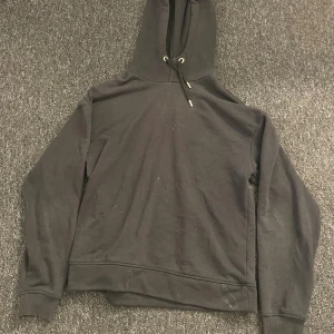 Svart hoodie från SOC med huva - Svart hoodie från SOC i storlek S. Tröjan har en klassisk huva med snörning och långa ärmar med ribbade muddar. Perfekt för chill eller träning, tillverkad i mjuk bomullsmix som är skön mot huden.