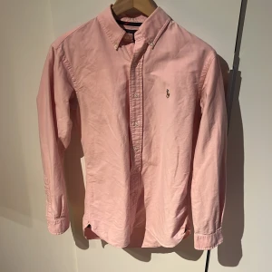 Rosa skjorta från Ralph Lauren - Snygg rosa skjorta storlek S från Ralph Lauren i bomull med klassisk button down-krage och broderad logga på bröstet. Perfekt för dig som gillar stilrena och tidlösa plagg. 