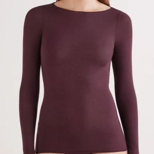 Mörklila långärmad topp - En stilren mörklila långärmad topp med rund halsringning. Toppen är figurnära och har en enkel, slät design utan synliga detaljer. Perfekt att matcha med jeans eller kjol för en clean look.