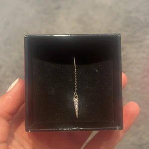 Silverörhänge med kedja från 184 Hasselblad - Snyggt och trendigt silverörhänge från L8 Hasselblad. Örhänget har en tunn kedja och en spetsig hängande detalj med små glittrande stenar. Perfekt för dig som gillar minimalistisk men ändå iögonfallande stil.