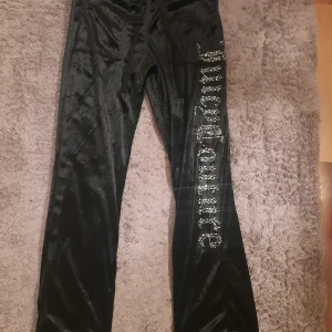Svarta Juicy Couture mjukisbyxor - Svarta mjukisbyxor från Juicy Couture i glansig sammet med stora cargofickor bak och snörning i midjan💕. Ena benet har Juicy Couture-loggan i glittrande stenar för extra bling. Perfekta för en chill och trendig look.❤️