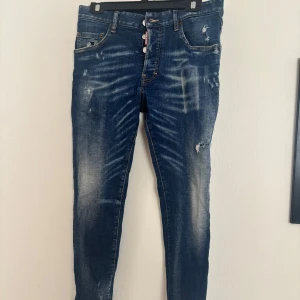 Dsquared2 jeans - Snygga blå jeans från Dsquared2 med små slitningar och distressed detaljer. Jeansen har slim passform, klassisk femficksdesign och synliga knappar framtill med Dsquared2-logga. Materialet är jeans med stretch och de har en cool, tvättad look. Knappt använda Storlek 46