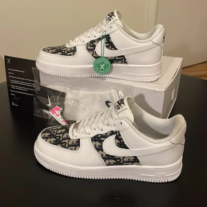 Nike Air Force 1 x dior - Nike Air Force 1 x dior sneakers i vitt skinn med svart och grått monogrammönster på tå och sidor. Klassisk låg modell med vit sula, snörning och ikonisk swoosh. Perfekt för dig som vill sticka ut med en unik och trendig look.  Provat skorna en två gånger tycke de bara inte var för mig. Bara höra av sig vid intresse. Nypris på dessa ligger på 3199
