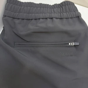 Grå mjukisbyxor från BOSS - Snygga grå mjukisbyxor från BOSS med elastisk midja och dragsko. Byxorna har diskret BOSS-logga bak, dragkedjeficka och raka ben. Perfekta för en chill och stilren look. Nypris: 1500kr