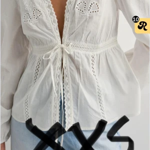 Amaze me blouse Nelly  - Säljer en söt vit blus i bomull med broderade detaljer och spets längs v-ringningen. Blusen har lång ärm, knyt i midjan och fina hålbroderier framtill. Slutsåld på hemsidan. Använd 1 kanske 2 gånger bara. 