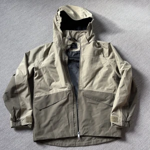 Everest - Ljusgrön/grön vindjacka med huva - Snygg grön vindjacka från Everest med justerbar huva och stora fickor framtill. Jackan har dragkedja hela vägen, kardborre vid ärmslut och reflekterande detalj bak. Perfekt för blåsiga dagar och outdoor-aktiviteter.