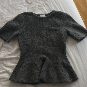 Mörkgrå stickad topp med kort ärm - Mysig mörkgrå stickad topp med korta ärmar och lätt utsvängd nederdel från H&M, använd 1 gång