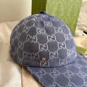 Blå Gucci keps med GG-mönster - Säljer en snygg blå keps från Gucci med det klassiska GG-monogrammet över hela kepsen. Kepsen har böjd skärm och en liten guldfärgad GG-detalj på sidan. Materialet är bomull och kepsen har en vit insida. Perfekt för dig som gillar exklusiva accessoarer.