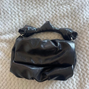Zara väska - Cool svart handväska i glansigt skinnimitation med unik knutdetalj på handtaget. 