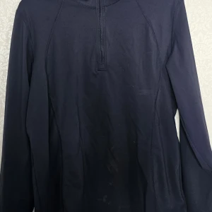 Mörkblå half zip tröja PS of Sweden - Sportig mörkblå långärmad tröja från PS of Sweden i storlek XL. Tröjan har half zip framtill och diskret logga på ryggen. Tillverkad i mjukt och stretchigt syntetmaterial, perfekt för ridning eller träning. Snygg passform och stilren design.