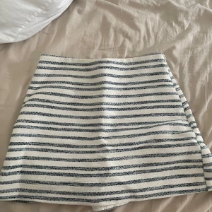 Randig kortkjol från Zara XS - Superfin kortkjol från Zara i storlek XS med vita och mörkblå ränder, den är inbyggd som shorts intill kjolen så man kan vara bekväm. Kjolen har en rak passform, dragkedja i sidan och är fodrad på insidan. Högmidjad. Perfekt för en classy look med en kavaj! Köpt från Frankrikes Zara!