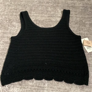 Svart stickad linnetopp med scallop-kant - Säljer en svart stickad linnetopp med breda axelband och snygg scallop-detalj längst ner. Toppen har en enkel, rak passform och är perfekt för att styla lager på lager eller till jeans. Mjuk och bekväm, passar dig som gillar en stilren look.