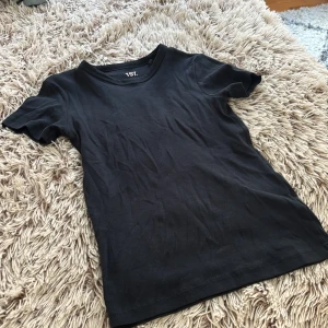 Svart ribbad t-shirt från 157, S - En svart ribbad t-shirt från 157 i storlek S. T-shirten är i mjuk bomullsblandning med 5% elastan för extra stretch och har klassisk rund hals och korta ärmar. Enkel och clean stil som funkar till allt.