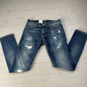 Nudie Jeans blå slim fit jeans - Snygga helt nya blå jeans från Nudie med lapparna kvar. slitna detaljer och lagningar på benen. Klassisk femficksmodell med orange sömmar på bakfickorna och slim fit passform (31 32). Men sitter mer som (30 30).