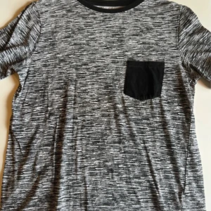 Svartvit t-shirt med ficka H&M - Svartvit mönstrad t-shirt från H&M i ekologisk bomull. T-shirten har korta ärmar, svart bröstficka och svart ribbad krage. Snygg och enkel stil som passar till det mesta.