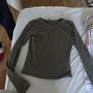 Olivgrön långärmad tröja från Nelly - En enkel och stilren olivgrön långärmad tröja från Nelly. Tröjan har rund halsringning och är figurnära i modellen, perfekt att matcha med jeans eller kjol. Tillverkad i mjuk bomull för en skön känsla hela dagen. Storlek XS