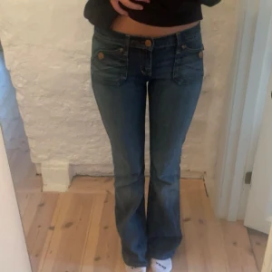 Blå bootcut jeans med låg midja - Jag är 168! Snygga blå jeans med bootcut-modell och låg midja. Jeansen har klassiska fickor fram och bak med snygga detaljer i form av kopparfärgade knappar. Perfekta för dig som gillar en retroinspirerad look och vill ha ett par jeans som sitter tajt upptill och släpper vid vaden.