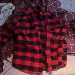 Röd och svart rutig skjorta Bluewear XL - Säljer en röd och svart rutig skjorta från Bluewear i storlek XL. Skjortan har klassisk krage, knappar framtill och två bröstfickor med knapp. Perfekt för dig som gillar avslappnad stil och rutigt mönster.