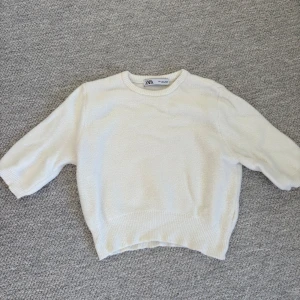 Vit stickad tröja från Zara - Säljer en vit stickad tröja från Zara med rund halsringning och ribbade muddar. Tröjan har kortare ärmar och en mjuk, mysig känsla. Perfekt för lager-på-lager.