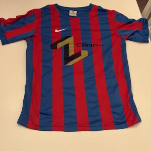 Nike Zlatan Ibrahimović fotbollströja L - Snygg fotbollströja från Nike med röda och blå vertikala ränder, gult Ibrahimović-tryck och nummer 9 på ryggen. Tillverkad i lätt och ventilerande Dri-Fit-material, perfekt för match eller träning. Klassisk rund hals och korta ärmar. Väldigt ovanlig tröja. 