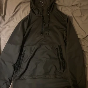 Nike Air Max svart hoodie med dragkedja - Svart Nike Air Max hoodie med halv dragkedja framtill och snörning i huvan. Stora fickor med dragkedja på magen och diskret Air Max-logga på bröstet. Tillverkad i mjukt syntetmaterial, perfekt för höst och vinter.