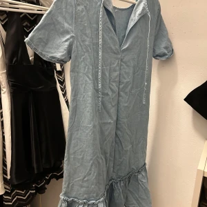 Ljusblå volangklänning med snörning - Supersöt ljusblå kortklänning i bomull med volang nertill och snörning vid halsen. Klänningen har korta ärmar och en avslappnad passform, perfekt för en chill sommardag. Enkel och stilren design som är lätt att matcha med sneakers eller sandaler.