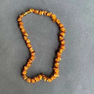 Halsband med bärnstensfärgade stenar - Unikt halsband med oregelbundna bärnstensfärgade stenar i varma orange och bruna toner. Stenarna är trätt på en tråd och halsbandet har ett klassiskt skruvlås. Perfekt för dig som vill sticka ut med ett naturligt och bohemiskt smycke.