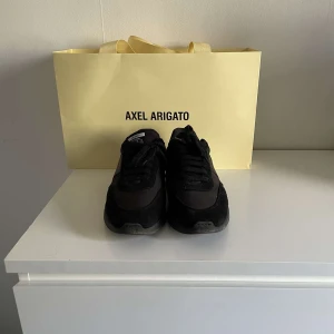 Svarta sneakers från Axel Arigato - Säljer ett par svarta sneakers från Axel Arigato med chunky sula och stilren design. Skorna har ovandel i en mix av skinn och mocka, med snörning och diskret logga på sidan. Perfekta för dig som gillar minimalistisk och modern streetstyle.