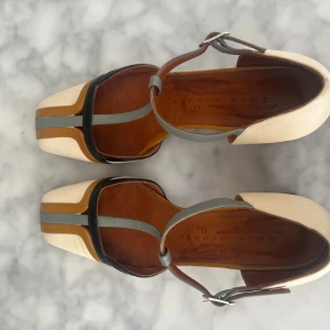 Chie Mihara sandaler med blockklack - Unika sandaler från Chie Mihara i beige, brunt, svart och grått skinn. Snygg design med T-rem, fyrkantig tå och blockklack med svartvita ränder. Perfekta för dig som vill sticka ut med coola detaljer och retrovibbar.