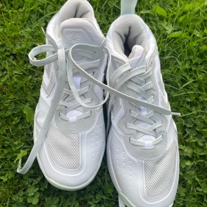 Vita sneakers från Hummel strl 37,5 - Snygga vita sneakers från Hummel i storlek 37,5. Skorna har en sportig design med meshpaneler och detaljer i syntetmaterial. Klassisk snörning och rund tå gör dem perfekta för en aktiv vardag. Hummels logga syns tydligt på sidan.