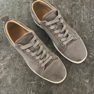 Loubs skor - Stilrena sneakers i grå mocka med vit sula och beige insida. Klassisk röd yttersula med bra grepp. Fint skick med mindre spår av användning. Passar både vardag och mer uppklädda tillfällen.