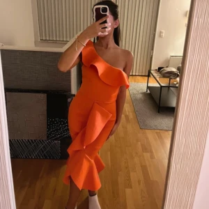 Volang klänning - En ursnygg orange festklänning med volanger som detalj. Klänningen är figursydd så den sätter sig perfekt efter ens kroppsform. Den är använd endast en gång! Den är i storlek S men kan även passa andra storlekar då den är i strech!💗