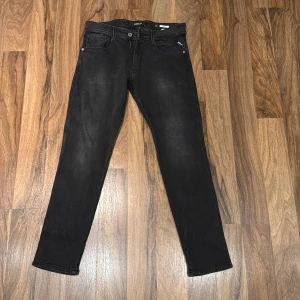Svarta Replay Anbass jeans 31/30 - Svarta Replay Anbass jeans med klassisk femficksdesign och dragkedjegylf. Jeansen har en slim passform och är tillverkade i mjukt denimtyg med lätt tvättad look. Snygga detaljer med Replay-logga på fickan och bakfickor med diskret söm.