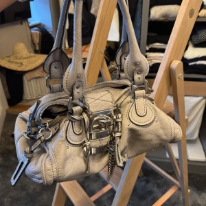 Chloé Paddington handväska i grå skinn - Cool beige Chloé Paddington handväska i mjukt skinn med chunky silverfärgade detaljer, ikoniskt hänglås och kedja med Zadig-berlock (kan köpas till för 200kr). Väskan har dubbla handtag, dragkedja upptill och flera snygga sömmar och nitar som ger en edgy vibe.