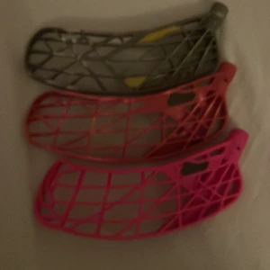 Innebandyklubba blad (3-pack) - Säljer tre innebandyklubba blad i olika färger (grå, röd, rosa). Bladen är lätt böjda och har synligt slitage, men är fortfarande funktionella. Perfekt för dig som vill byta ut eller testa olika blad till din klubba. Inga större sprickor eller defekter syns.