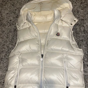 Vit dunväst från Moncler - Snygg vit dunväst från Moncler. Västen har två dragkedjefickor. Man kan ta av luvan om man vill. Taggar och allt finns. Aldrig använd helt ny. Pris kan diskuteras vid snabb affär 