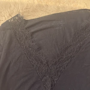 Svart långärmad klänning med spets - Svart långärmad klänning från Intimissimi med v-ringad hals och dekorativ spets längs halsringningen och ärmsluten. Mjuk och följsam passform, perfekt för dig som gillar stilrena detaljer och en feminin look.