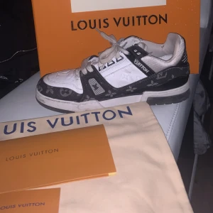 Louis Vuitton sneakers svart/vit monogram - Säljer ett par Louis Vuitton sneakers i svart och vitt med klassiskt monogrammönster. Skorna har snörning, platt sula och rund tå. Materialmix av skinn och textil med tydliga LV-detaljer på sidan och hälen. Riktigt snygga och exklusiva sneakers för dig som gillar streetstyle. Dom måste bara tvättas