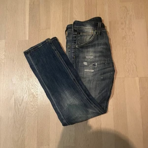 Jack and Jones jeans - Snygga blå Jack and Jones jeans modell Slim Glenn storlek 27/30. Jeansen har feta slitningar, Klassisk femficksmodell med knapp. Jeansen är använda men i fint skick