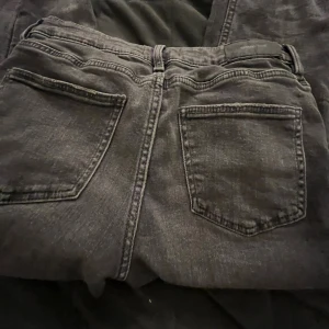 Grå  jeansbyxor från Gina Tricot - Säljer ett par svarta jeansbyxor från Gina Tricot i storlek 152. Klassisk femficksmodell med bälteshällor och knappstängning. Jeansen har en något tvättad look och raka ben, perfekta för en avslappnad stil.