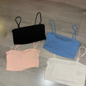 Fem toppar från H&M Divided - Säljer ett set med fyra bandeau toppar från H&M Divided i storlek XS. Färgerna är svart, ljusblå, ljusrosa och vit. Alla toppar har smala axelband utom den ljusrosa som är axelbandslös. Perfekta för sommaren och att styla lager på lager. Den sista toppen är i storlek xxs